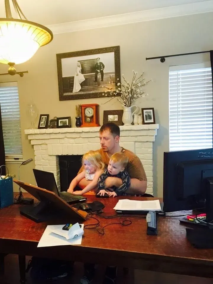 Work and family — never far from each other. Mark C. Smith working at his home desk with one of his young children seated on his lap.