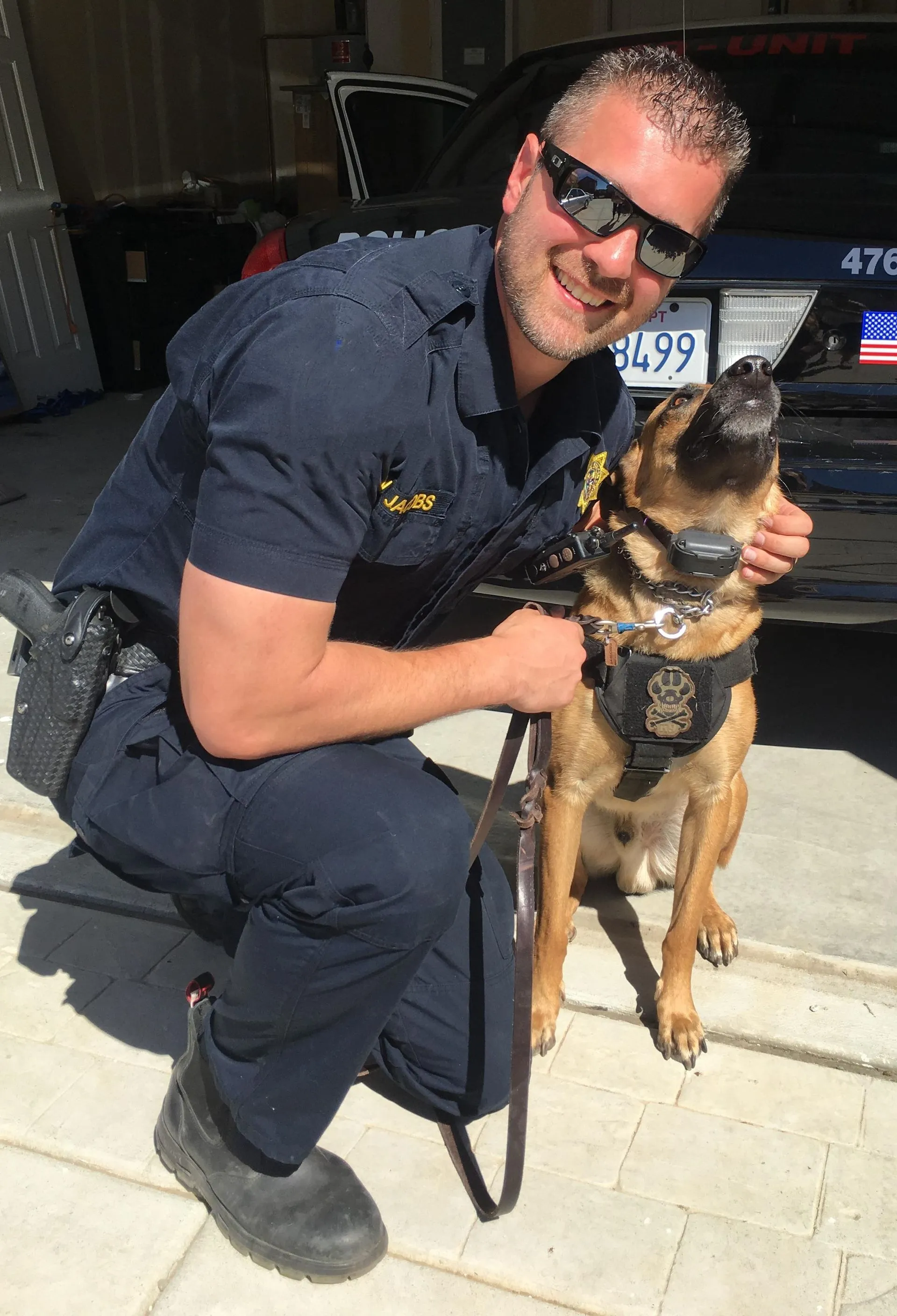 On patrol with his K9 partner. Nicholas Jacobs in police uniform kneeling beside his canine partner alongside a police vehicle.